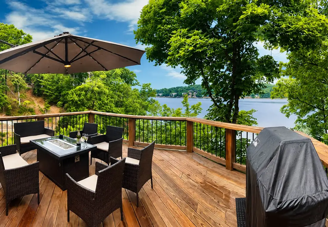 The lakefront deck in the sun, with a fire table, seating, umbrella and grill