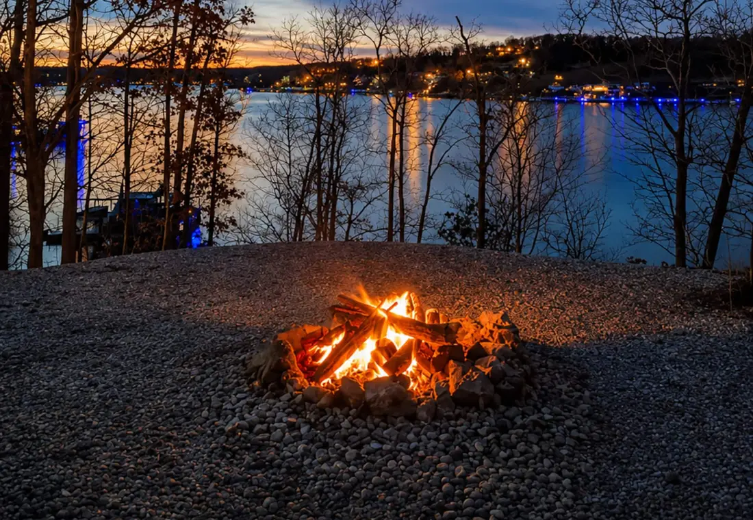 The fire pit burning at blue hour, with the lake and far shore lights beyond
